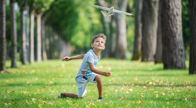 boy-playing-with-toy-glider-in-park-on-summer-day-PTXPHJC